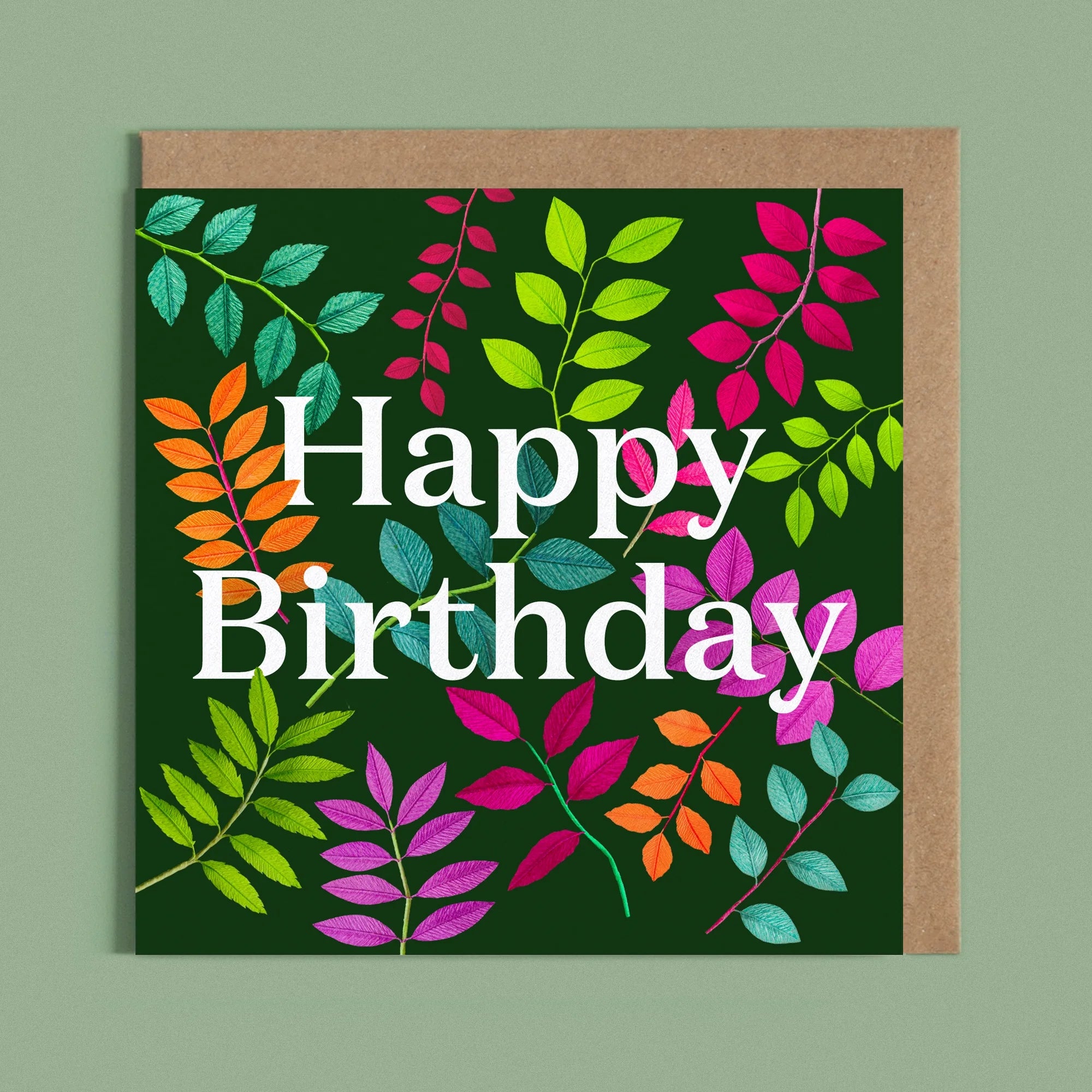 Greeting card with a image of a white Happy Birthday and colourful handcrafted paper foliage on a dark green background by paper artist Daphne Fitch.