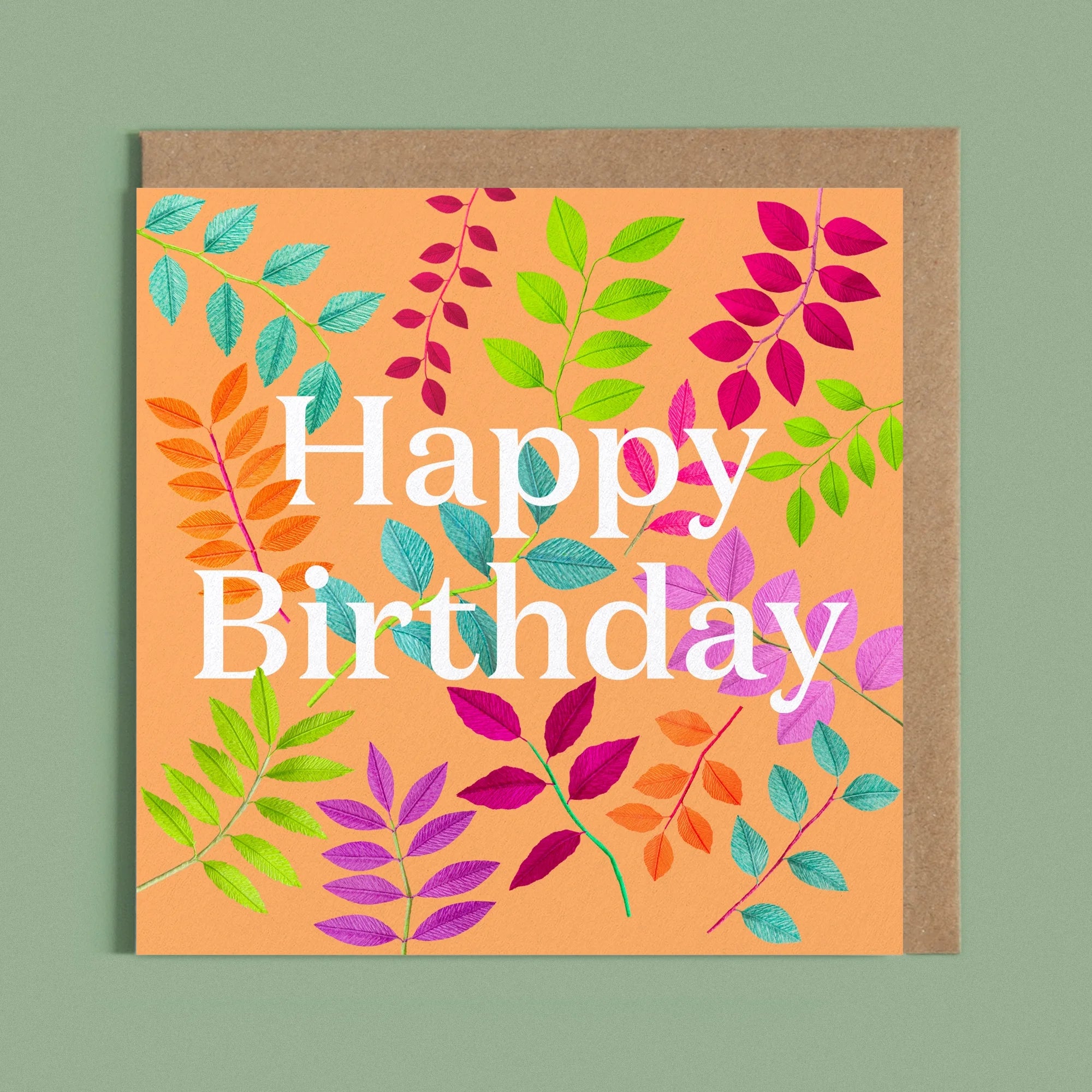 Greeting card with a image of a white Happy Birthday and colourful handcrafted paper foliage on a orange background by paper artist Daphne Fitch.