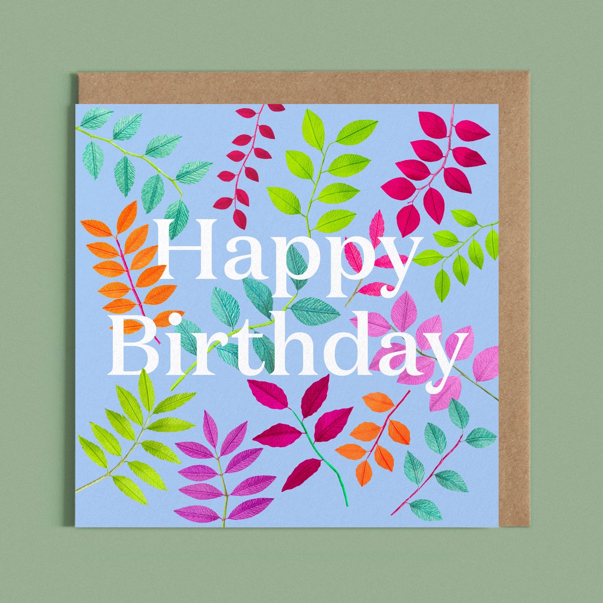 Greeting card with a image of a white Happy Birthday and colourful handcrafted paper foliage on a blue background by paper artist Daphne Fitch.