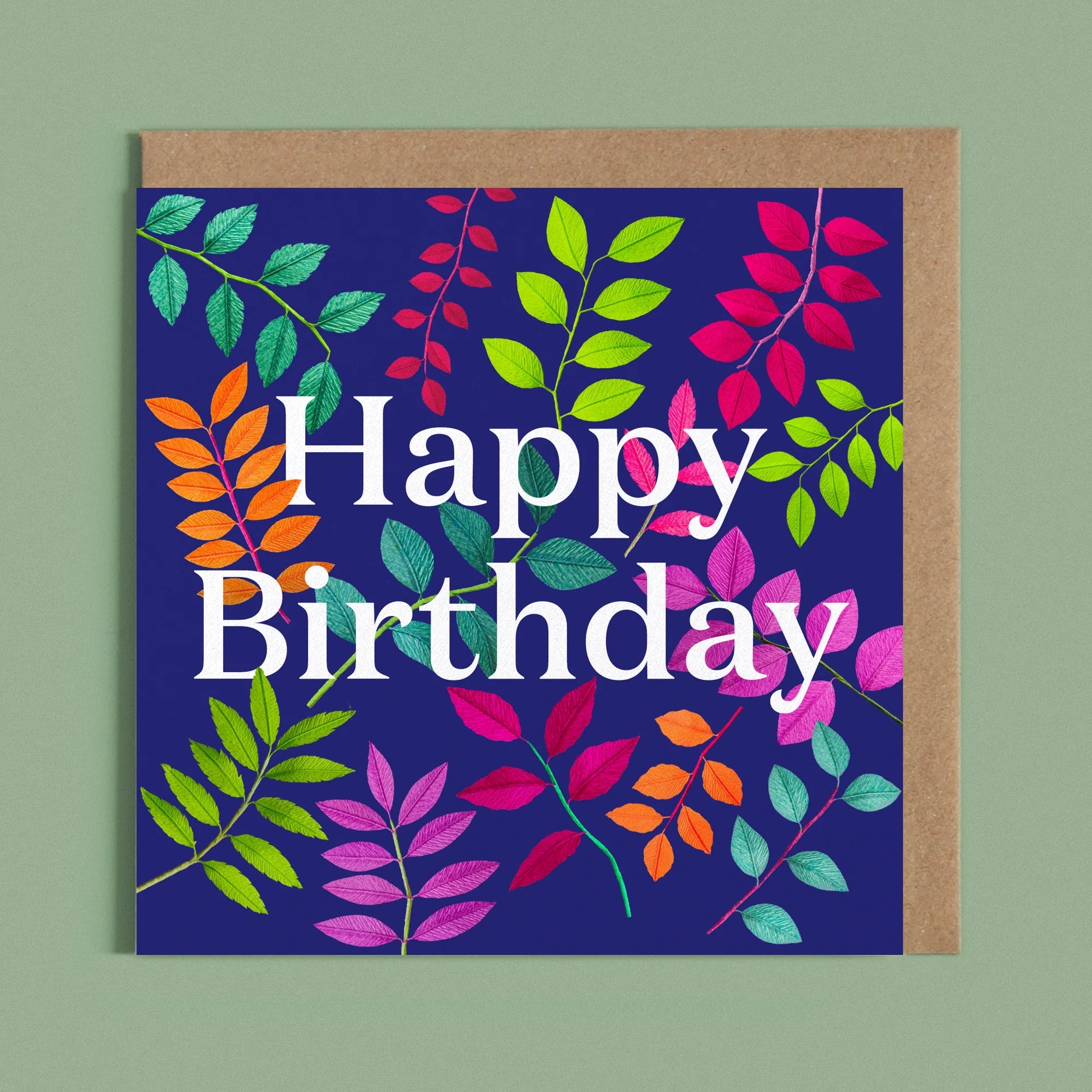 Greeting card with a image of a white Happy Birthday and colourful handcrafted paper foliage on a dark blue background by paper artist Daphne Fitch.