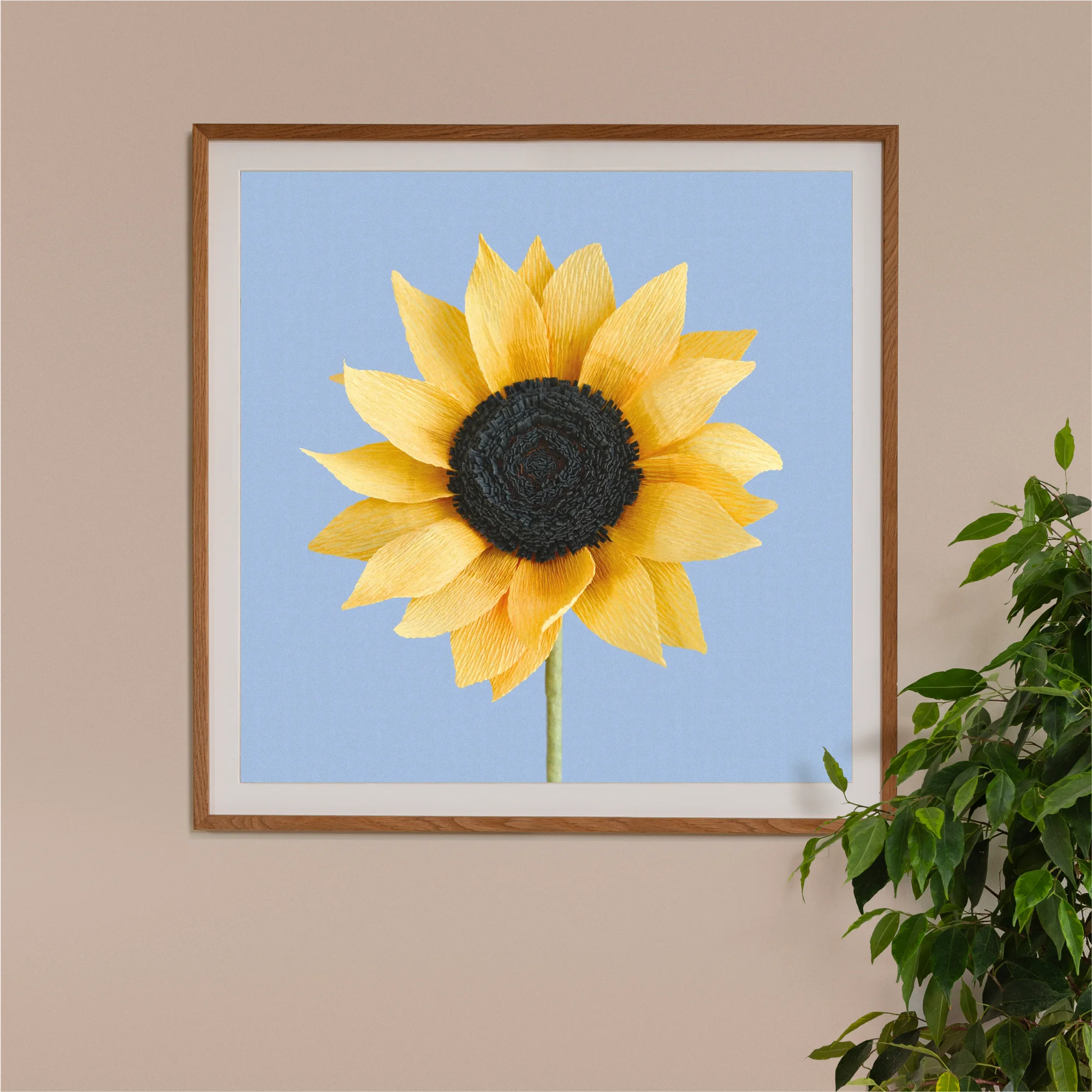 Image of framed art print on a wall, featuring handcrafted paper sunflower on a blue background. Created by paper artist Daphne Fitch.