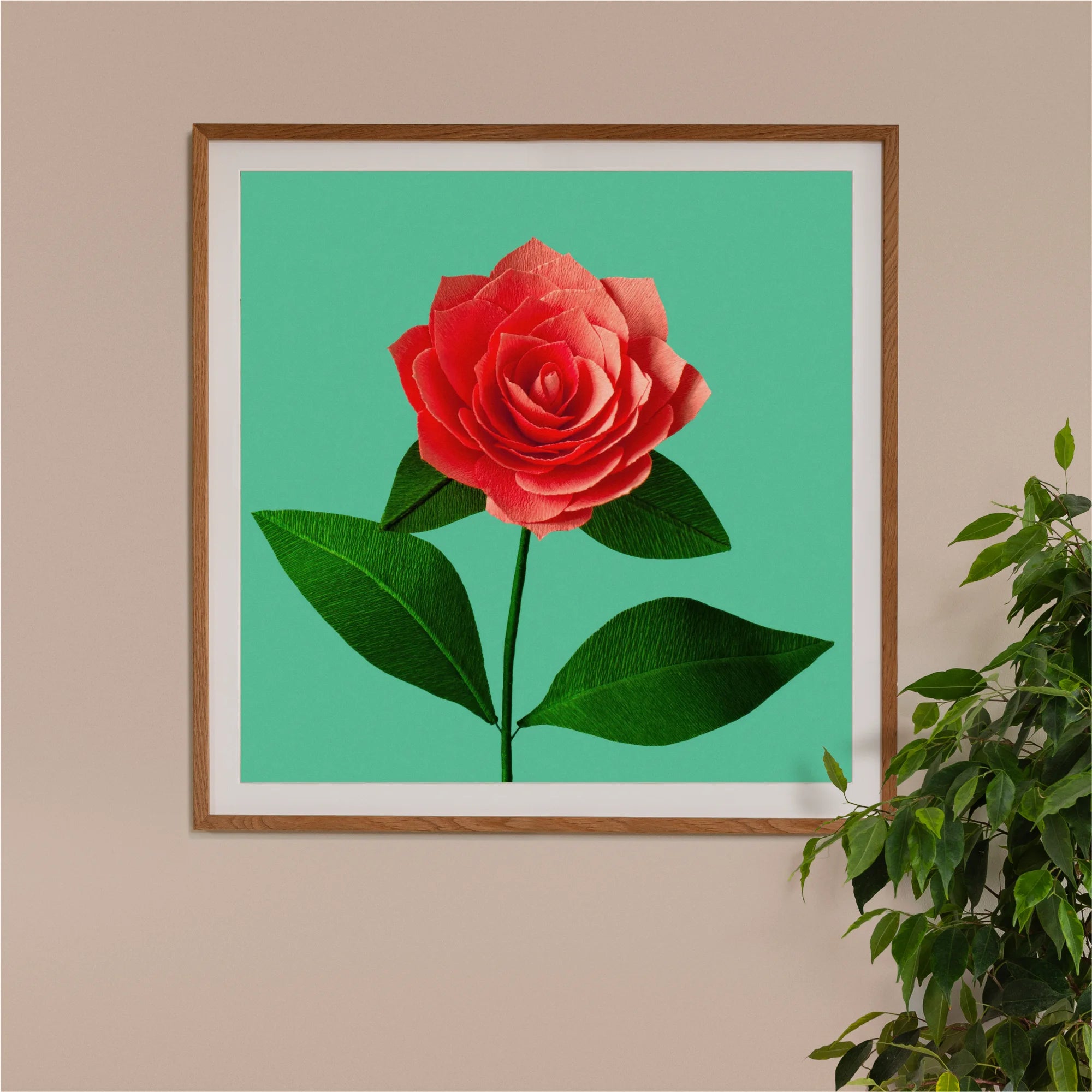 Image of framed art print on a wall, featuring handcrafted paper coral camellia on a green background. Created by paper artist Daphne Fitch.