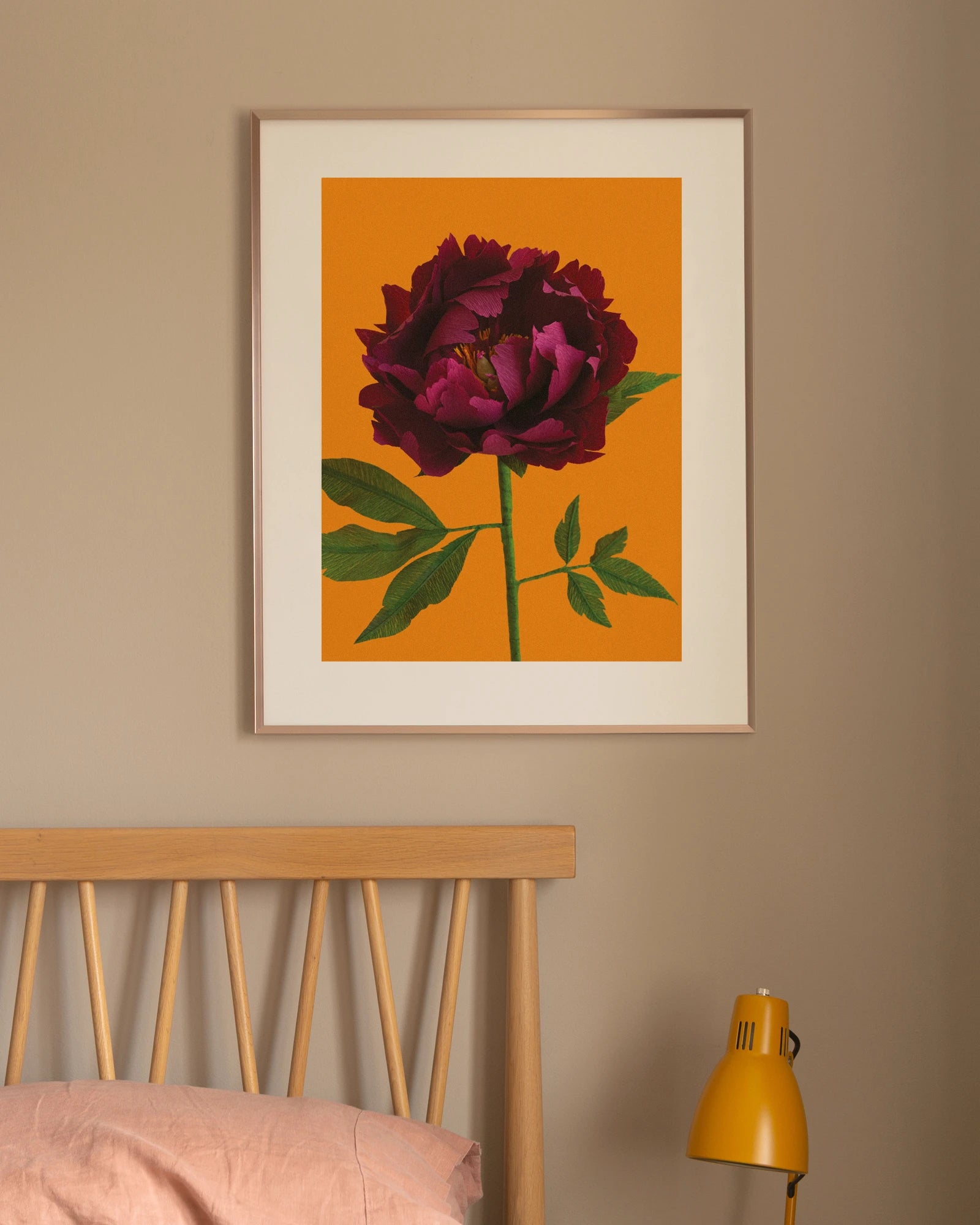 Image of framed art print on a bedroom wall, featuring handcrafted paper peony on a orange background. Created by paper artist Daphne Fitch.