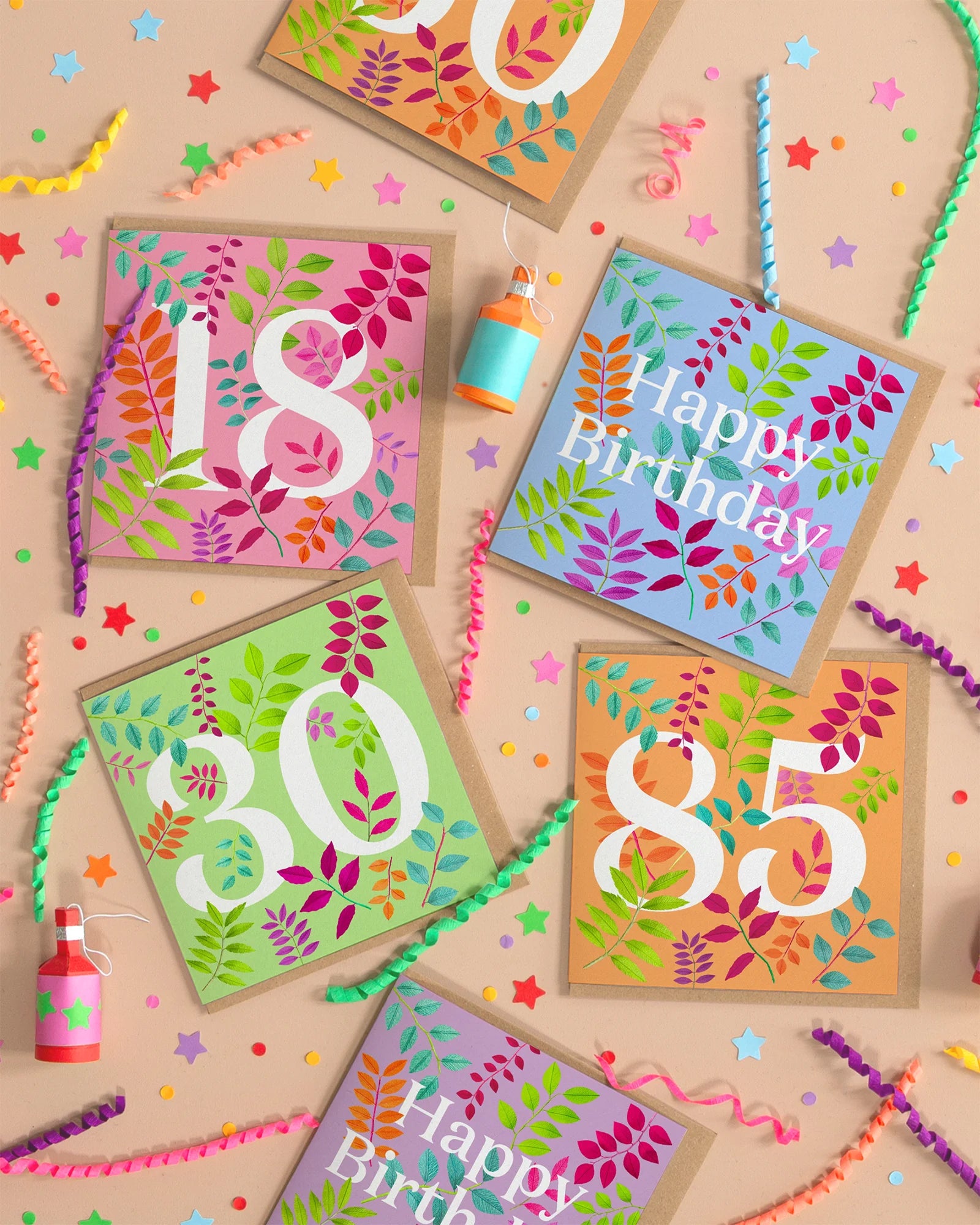 Image of an assortment of celebration birthday cards on a peach background colour featuring hand crafted paper foliage. Created by paper artist Daphne Fitch.