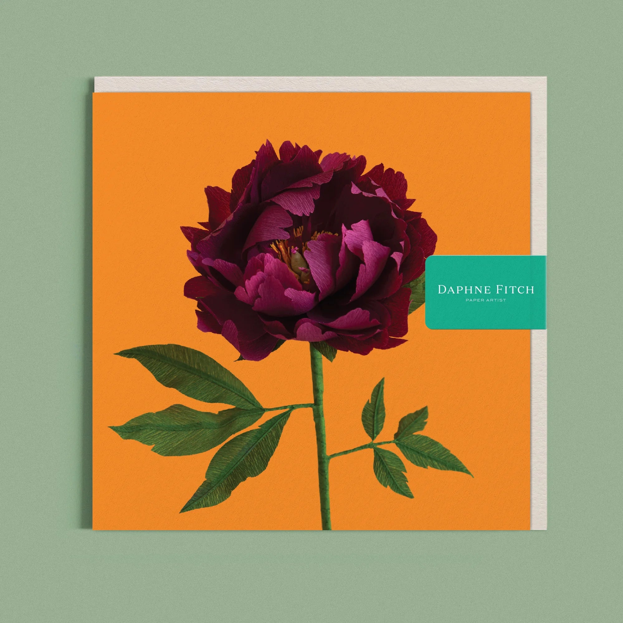 Greeting card with a image of a handcrafted paper red peony on a marigold background by paper artist Daphne Fitch.
