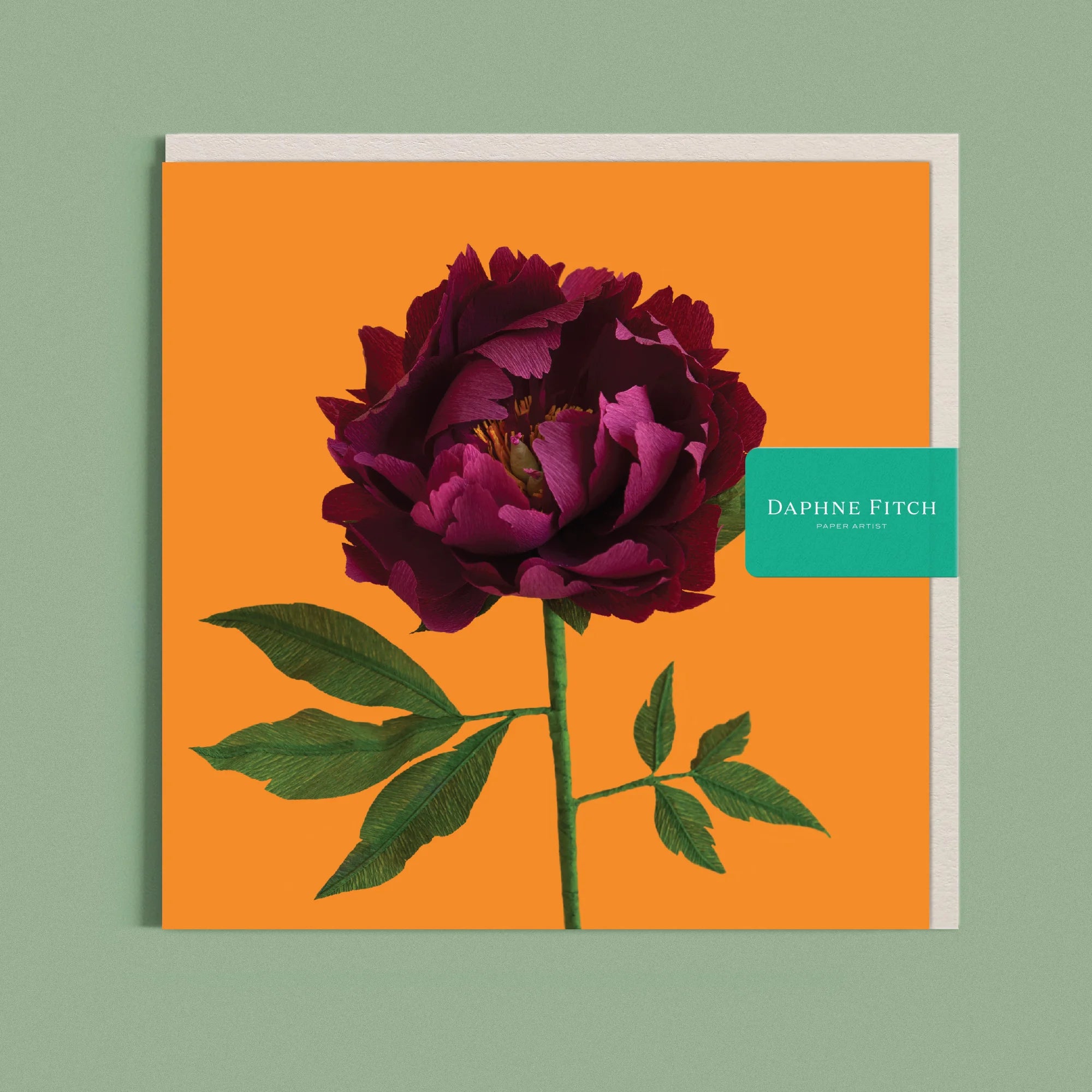 Greeting card with a image of a handcrafted paper peony garnet red on a marigold background by paper artist Daphne Fitch.