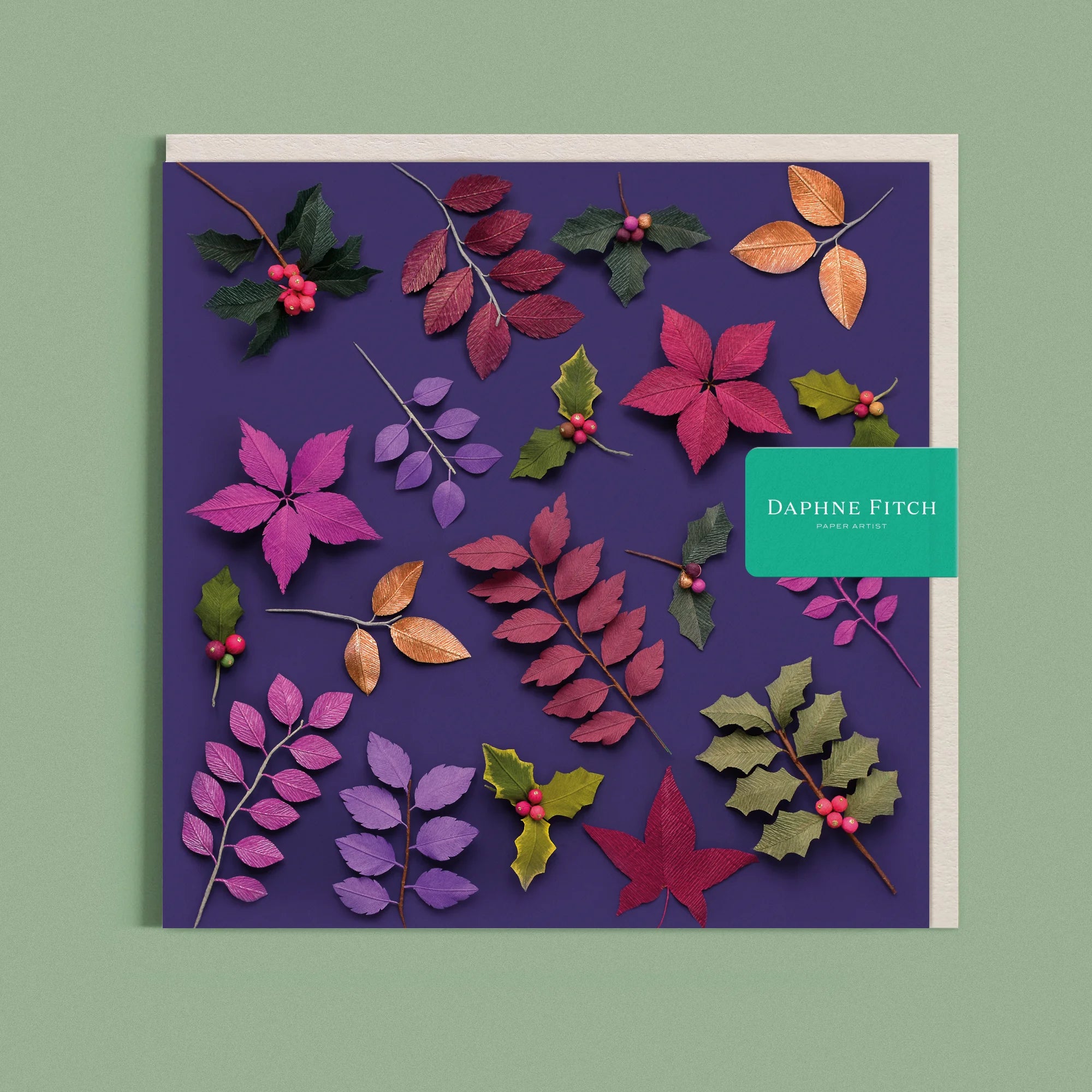 Greeting card with a image of a handcrafted paper holly leaves and berries on a purple background by paper artist Daphne Fitch.