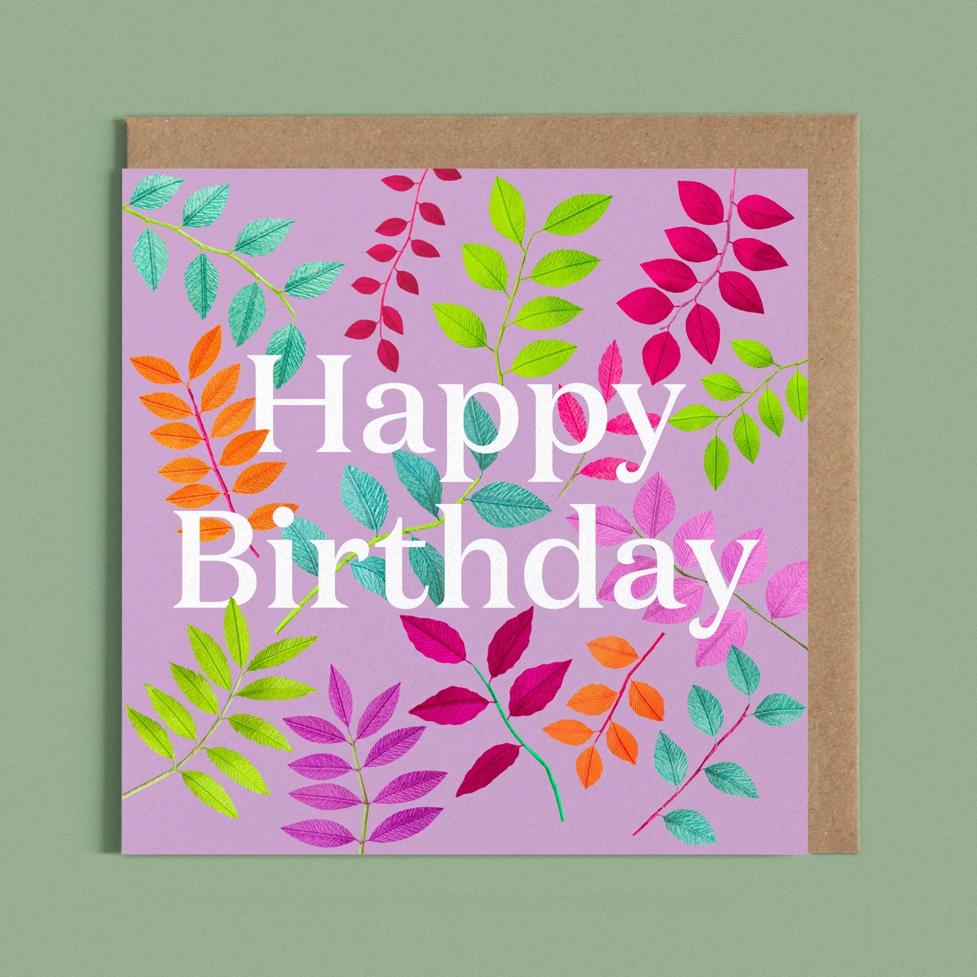 Greeting card with a image of a white Happy Birthday and colourful handcrafted paper foliage on a light pruple background by paper artist Daphne Fitch.