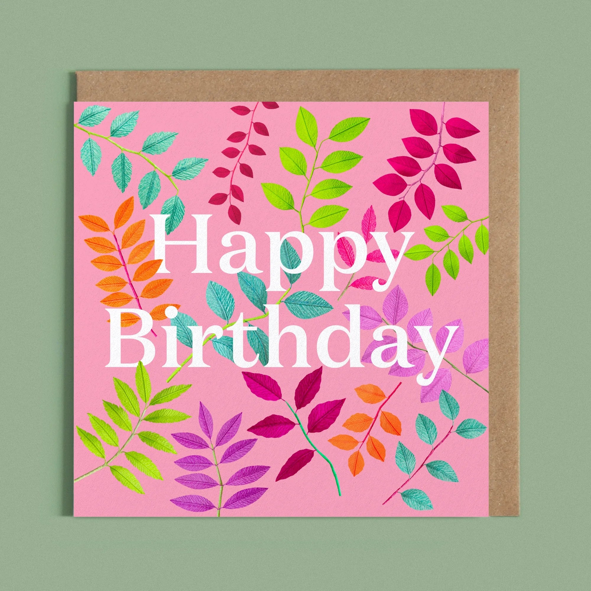 Greeting card with a image of a white Happy Birthday and colourful handcrafted paper foliage on a pink background by paper artist Daphne Fitch.