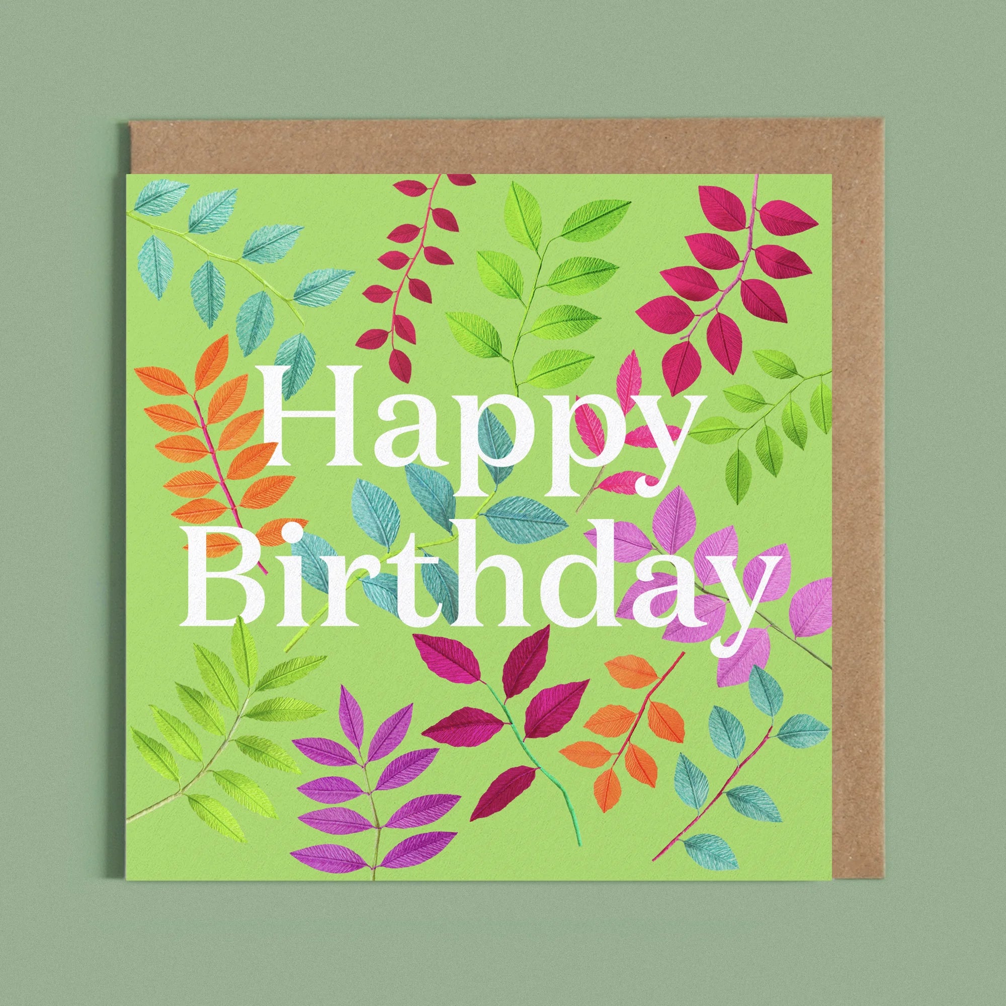 Greeting card with a image of a white Happy Birthday and colourful handcrafted paper foliage on a green background by paper artist Daphne Fitch.