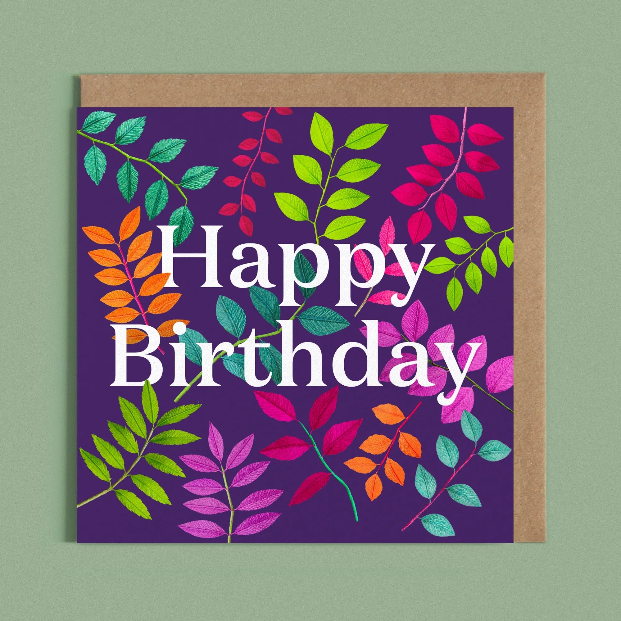 Greeting card with a image of a white Happy Birthday and colourful handcrafted paper foliage on a dark purple background by paper artist Daphne Fitch.