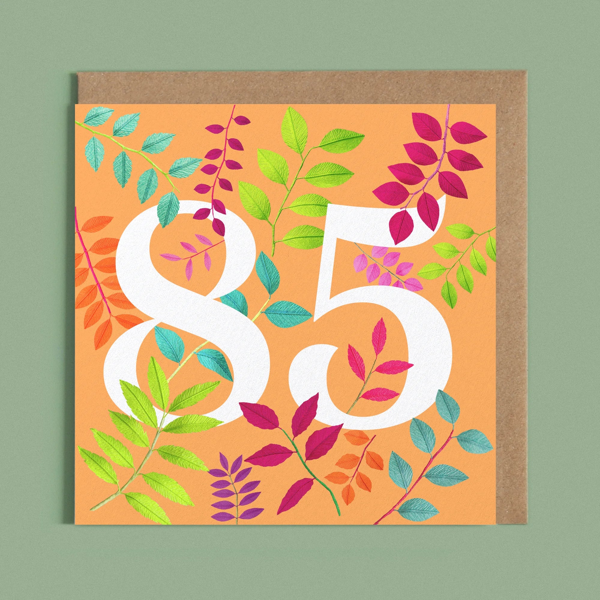 Greeting card with a image of a white number 85 and colourful handcrafted paper foliage on a orange background by paper artist Daphne Fitch.