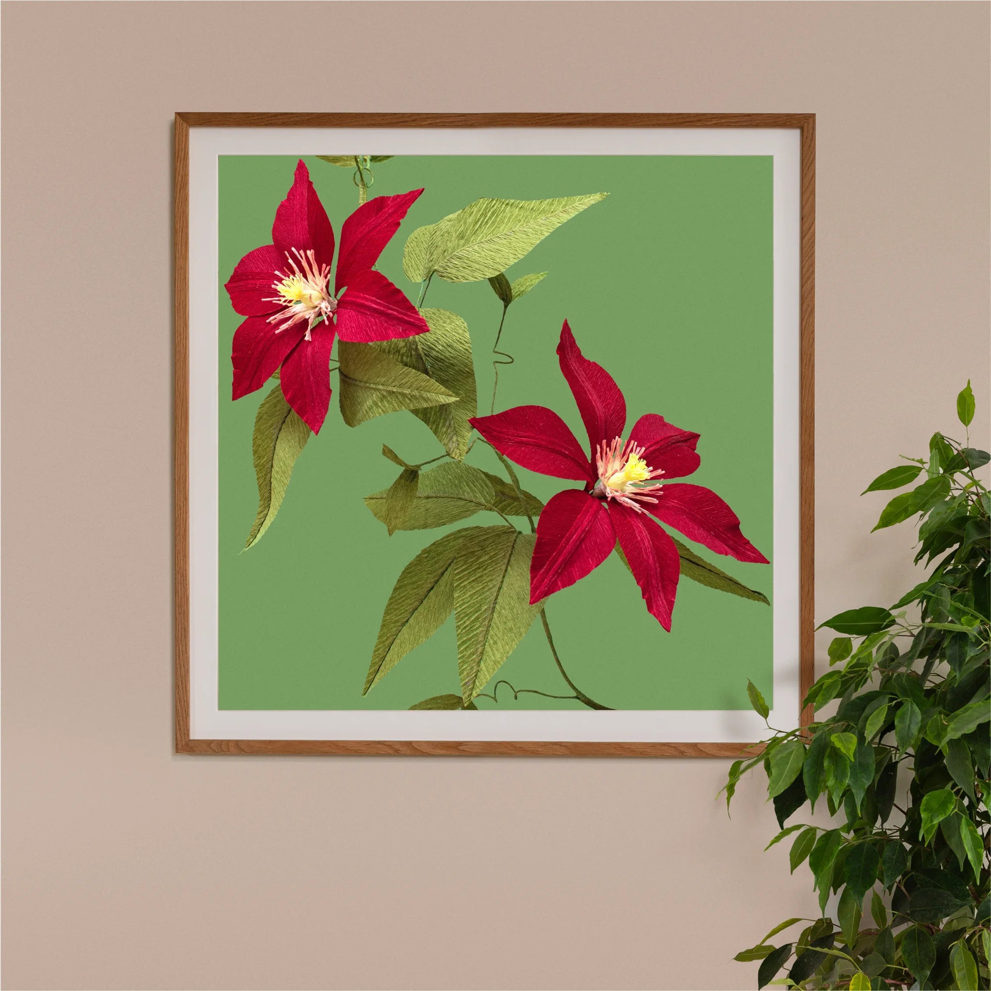 Image of framed art print on a wall, featuring handcrafted paper red clematis on a green background. Created by paper artist Daphne Fitch.