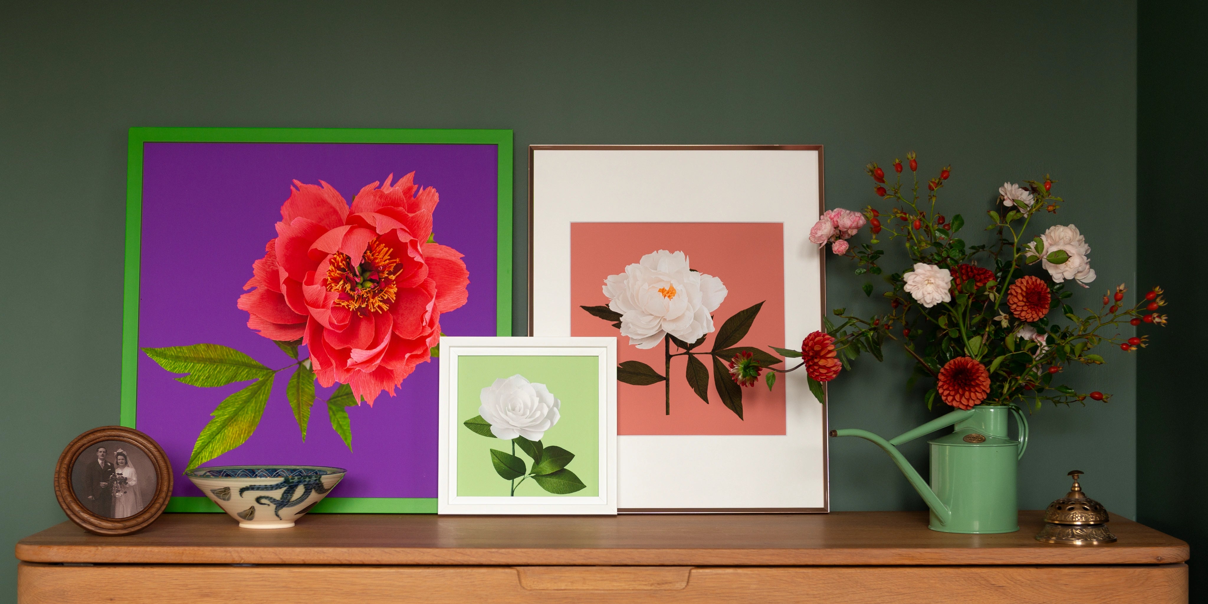 Image of various art prints in frames featuring handcrafted paper flowers on a sideboard by paper artist Daphne Fitch.