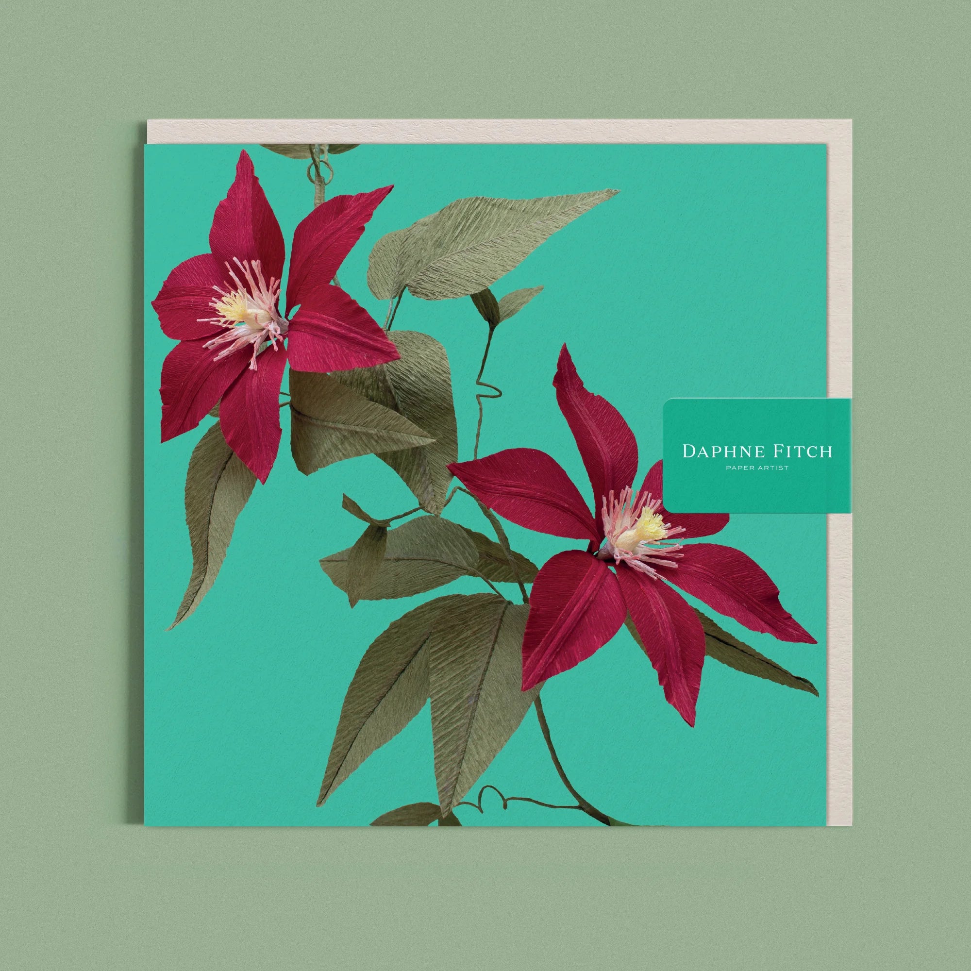 Greeting card with a image of a handcrafted paper red camellia on a green background by paper artist Daphne Fitch.
