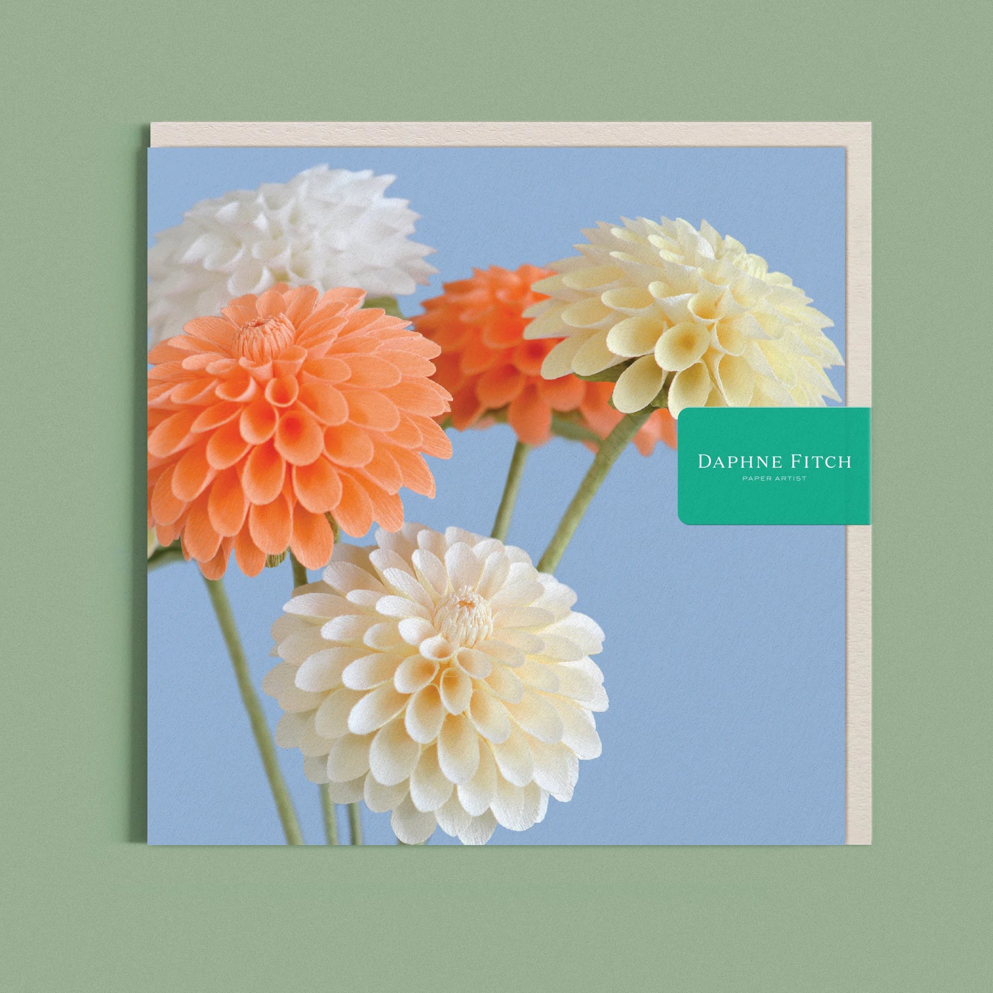 Greeting card with a image of a handcrafted paper cream and peach dahlia on a blue background by paper artist Daphne Fitch.
