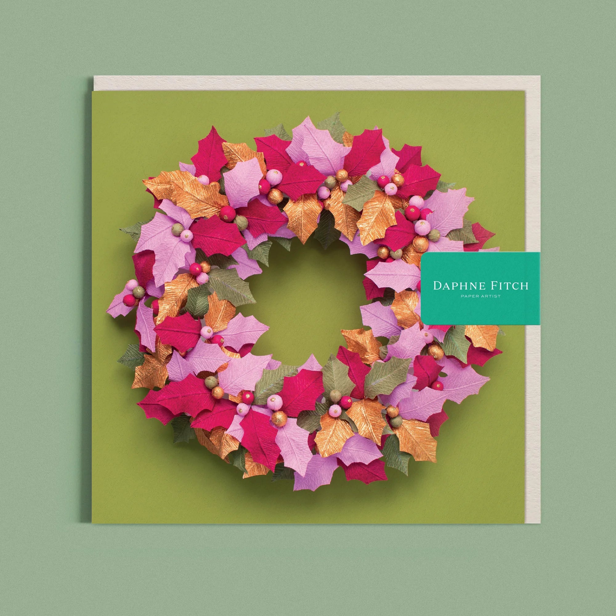 Greeting card with a image of a handcrafted paper holly wreath on a green background by paper artist Daphne Fitch.