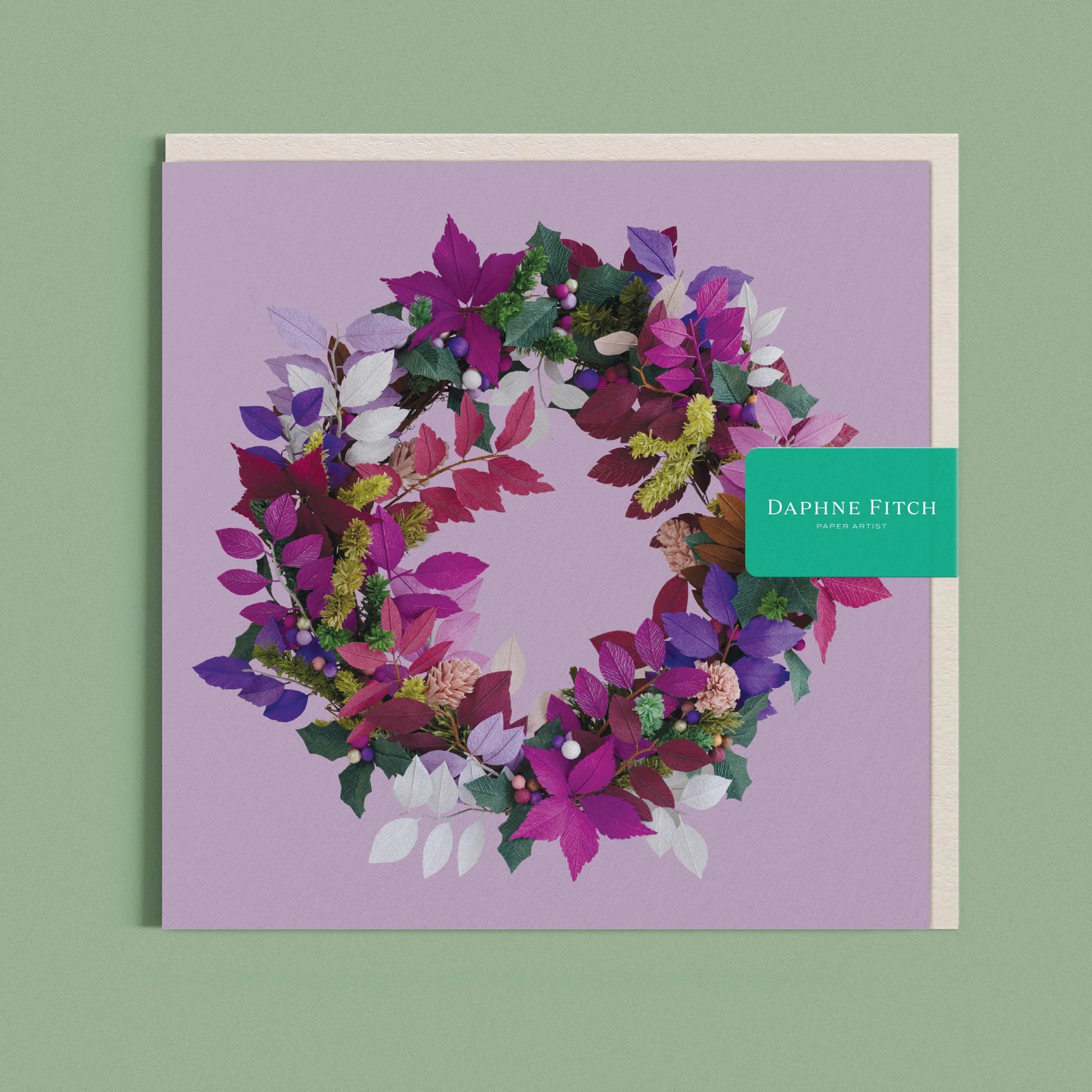 Greeting card with a image of a handcrafted paper holly wreath on a purple background by paper artist Daphne Fitch.